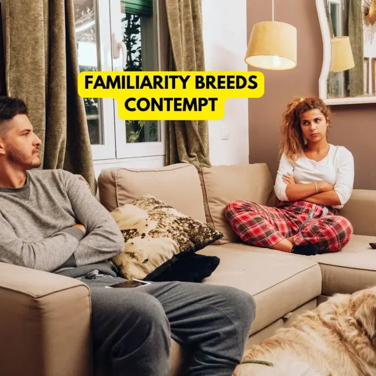 A man and a woman sit on a couch in a living room, both appearing upset with arms crossed and looking away from each other. A